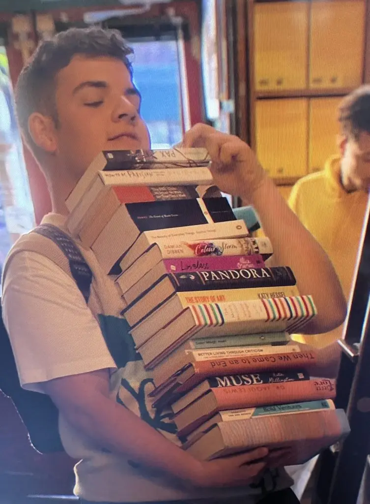 Isaac from Heartstopper with a pile of books he is buying in Paris